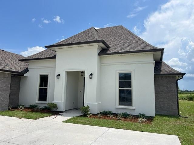 A single-story white house with dark gray trim and a brick side wall under a bright blue sky with scattered clouds.