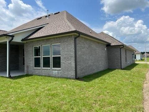 A light gray brick house with a dark shingled roof under a blue sky with clouds, seen from a grassy yard.
