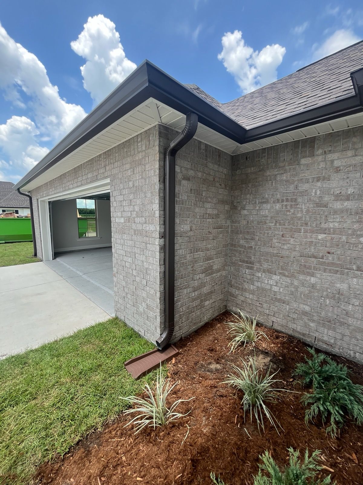 Corner view of a brick house exterior with dark gutters, a garage opening, and a mulched garden bed in the foreground.