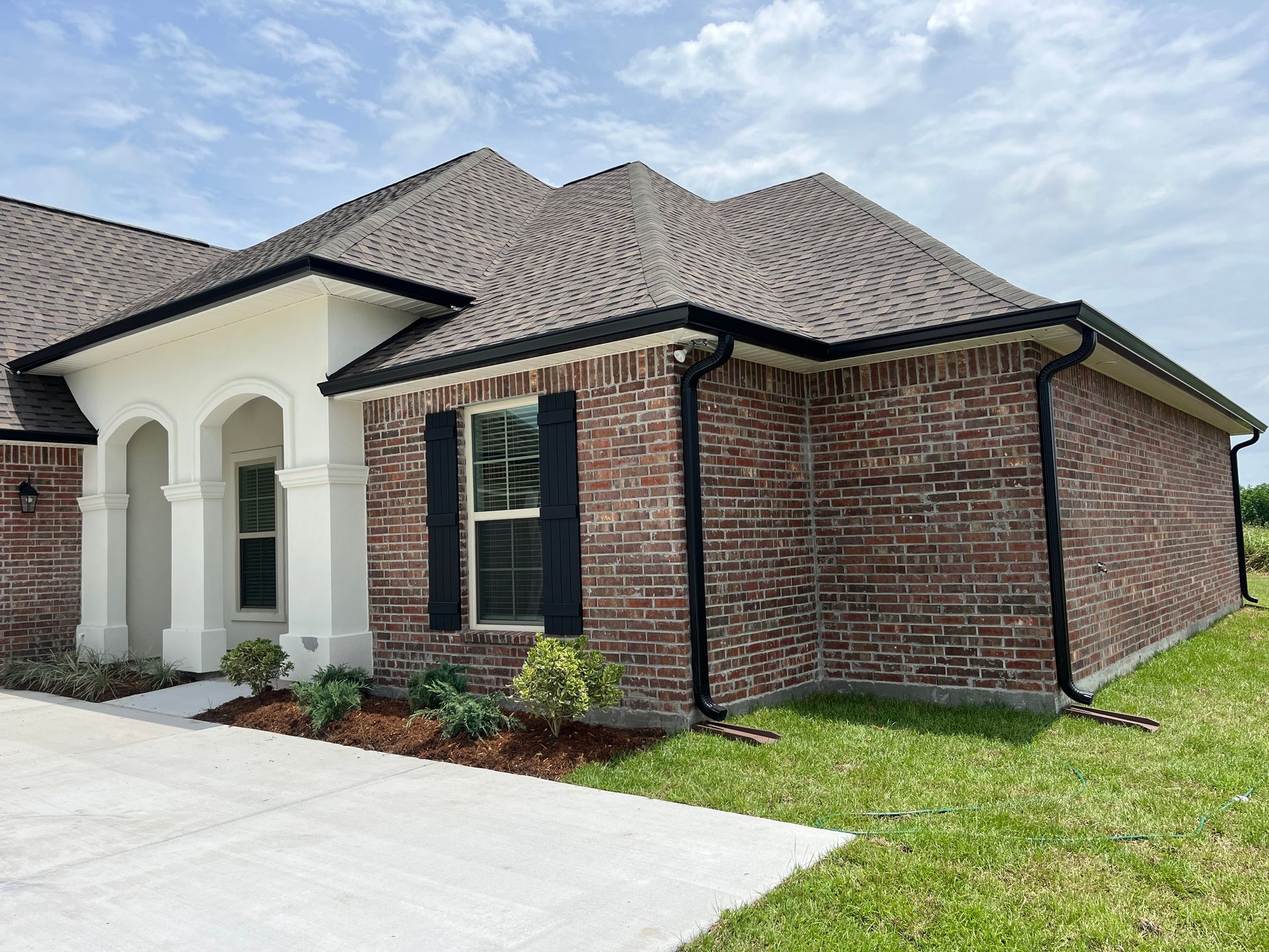 A single-story brick house with a light stucco entryway, dark shutters, and a dark shingle roof, set on a grassy lawn.