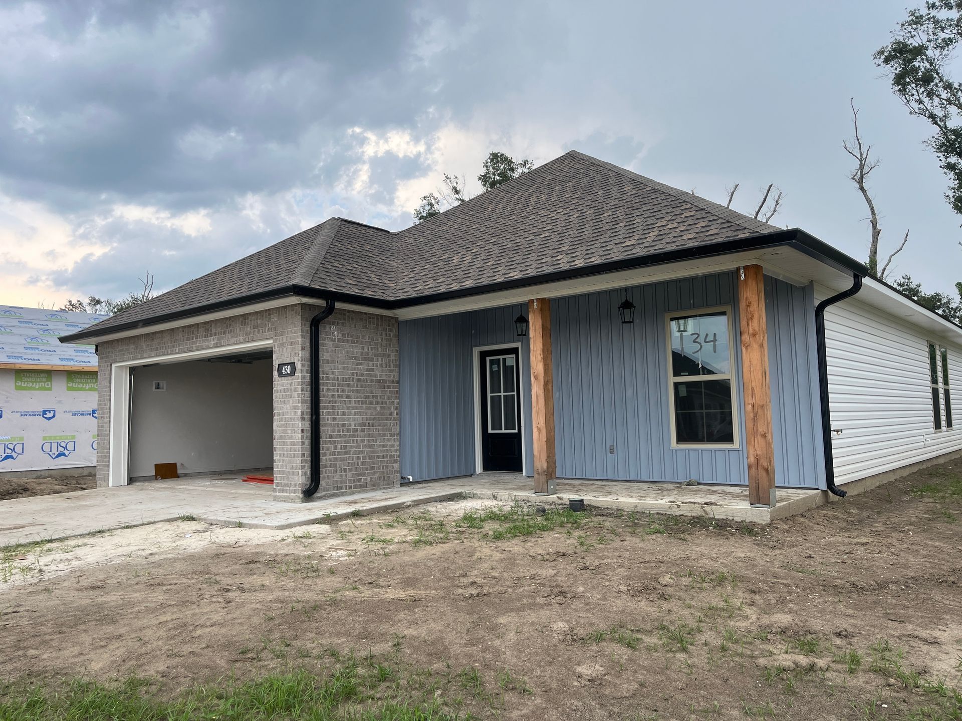 A newly constructed single-story house with a brick garage, light blue vertical siding, and two wooden porch posts.