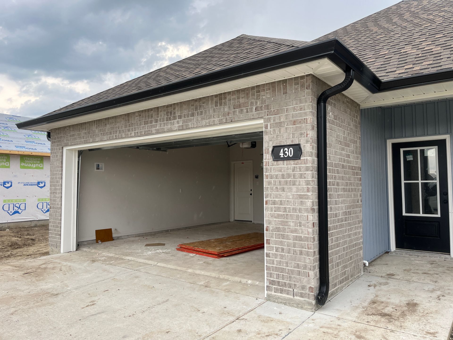 Exterior of a modern brick-and-siding house under construction, featuring an open garage and a black-framed front door.