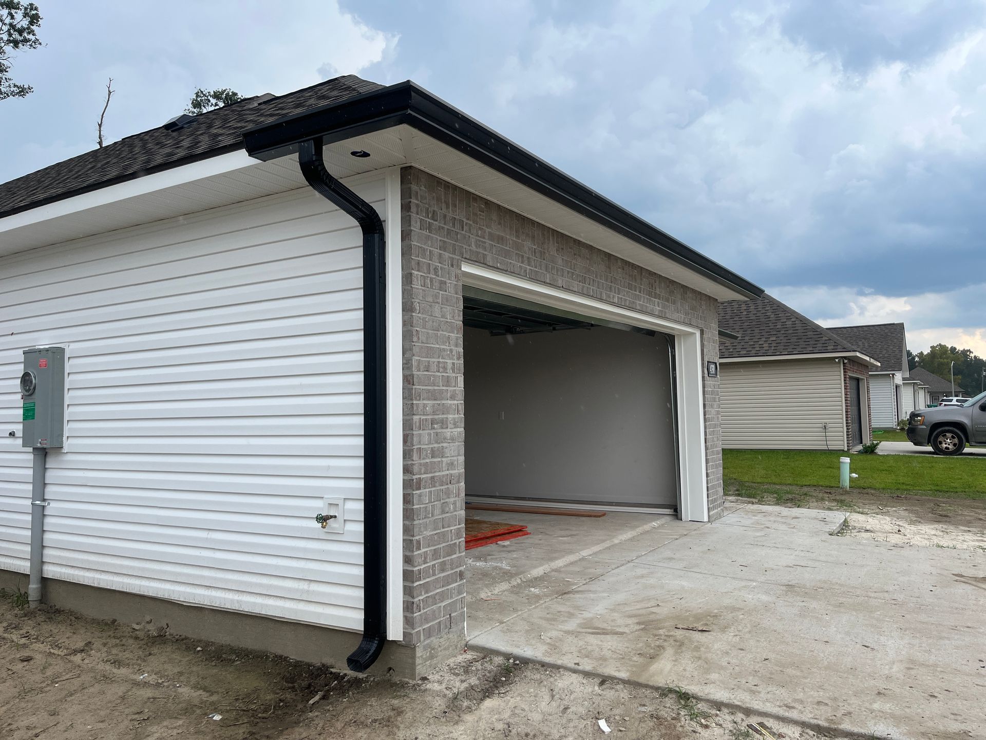 A side view of a residential garage with white vinyl siding, a brick front, a black gutter downspout, and a gray interior.