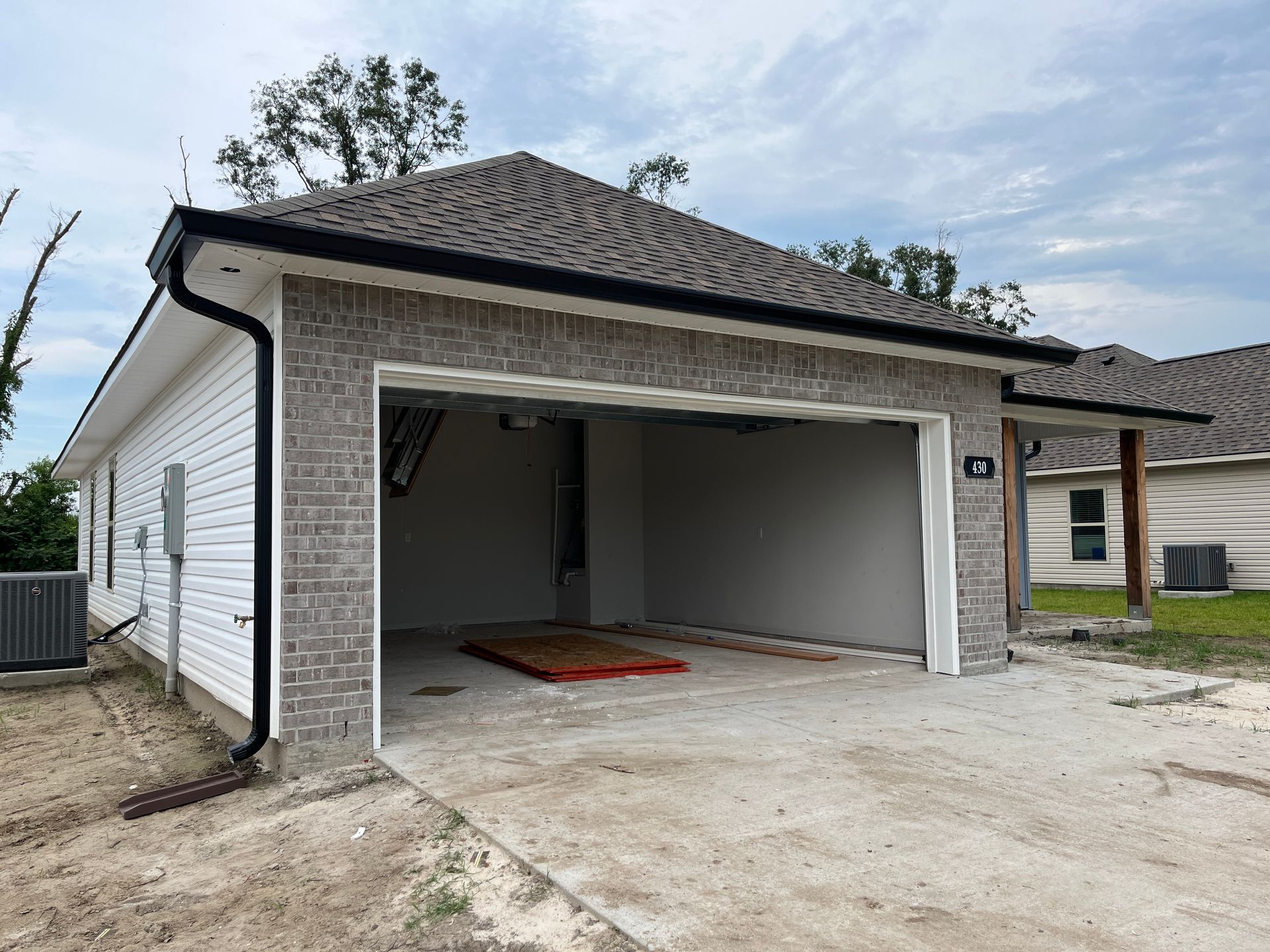 A newly constructed house with gray brick, white siding, and a large, open garage bay under a dark shingled roof.