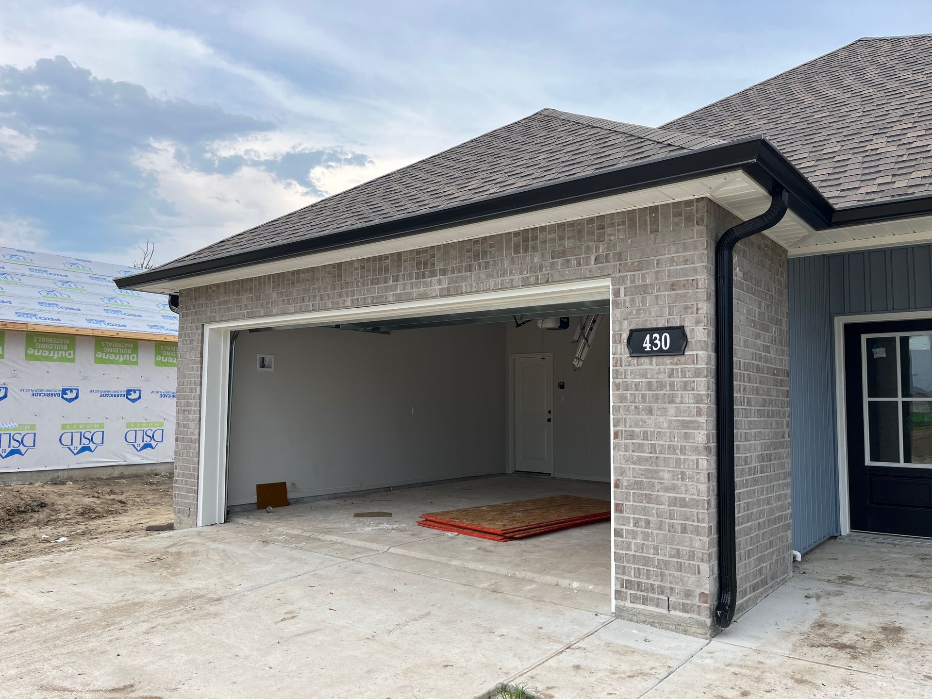 A modern single-story house under construction with a brick exterior, open garage, and a black front door.