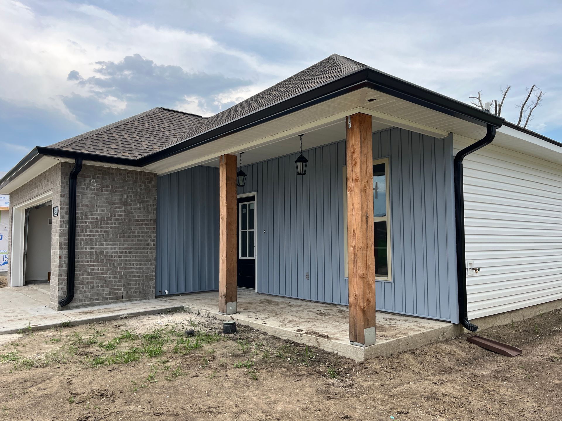 A modern house with a front porch, featuring grey brick, light blue vertical siding, wood posts, and white siding.