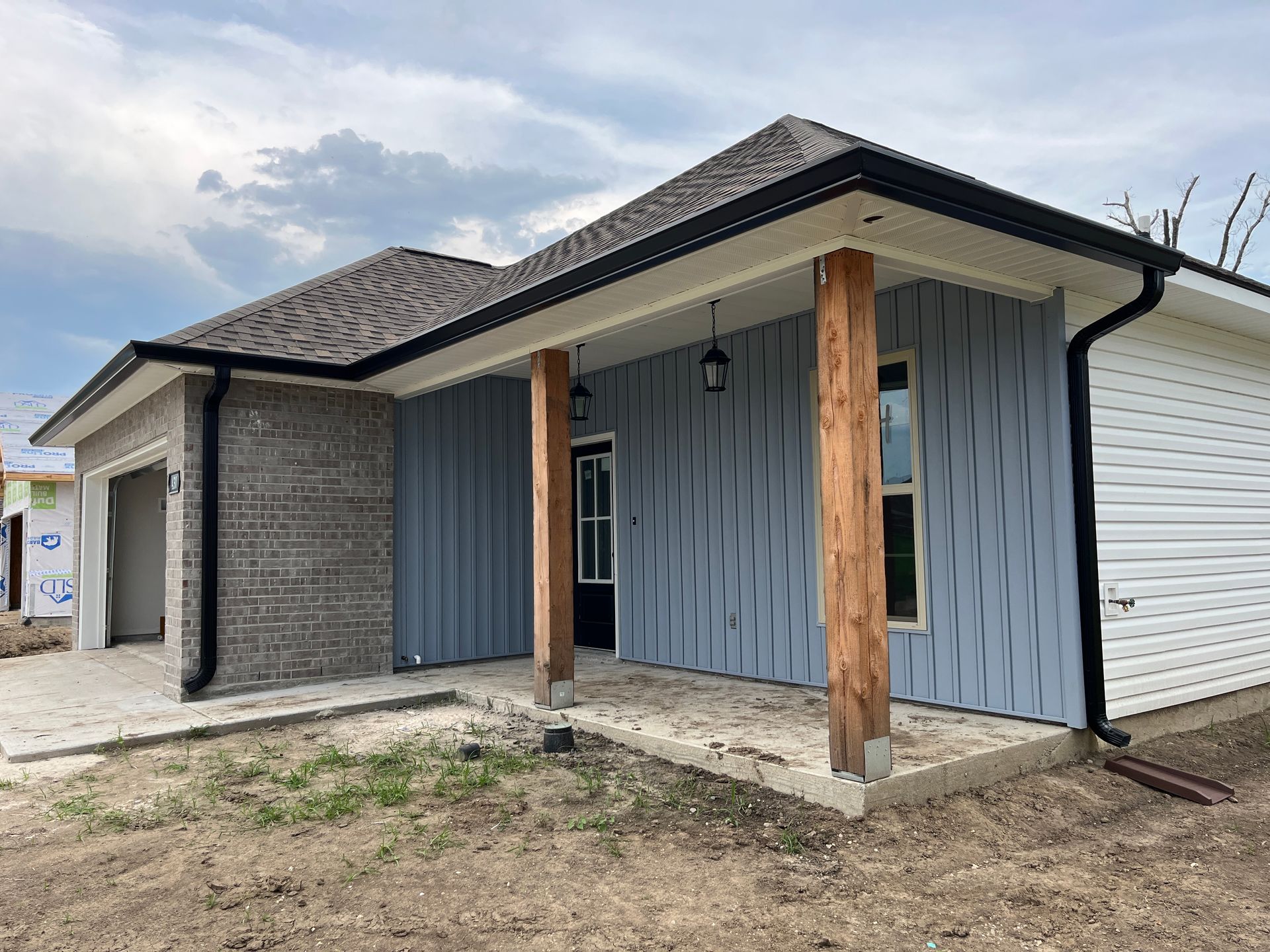 A modern single-story house with a brick garage, blue vertical siding, and a covered porch with rustic wooden pillars.