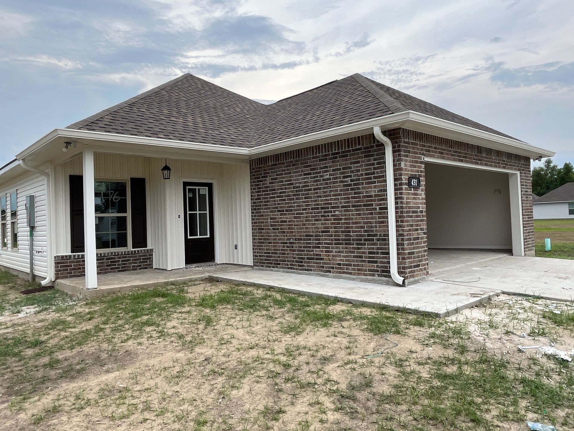 A newly constructed, single-story house with a brick exterior, a grey shingled roof, a front porch, and a garage.