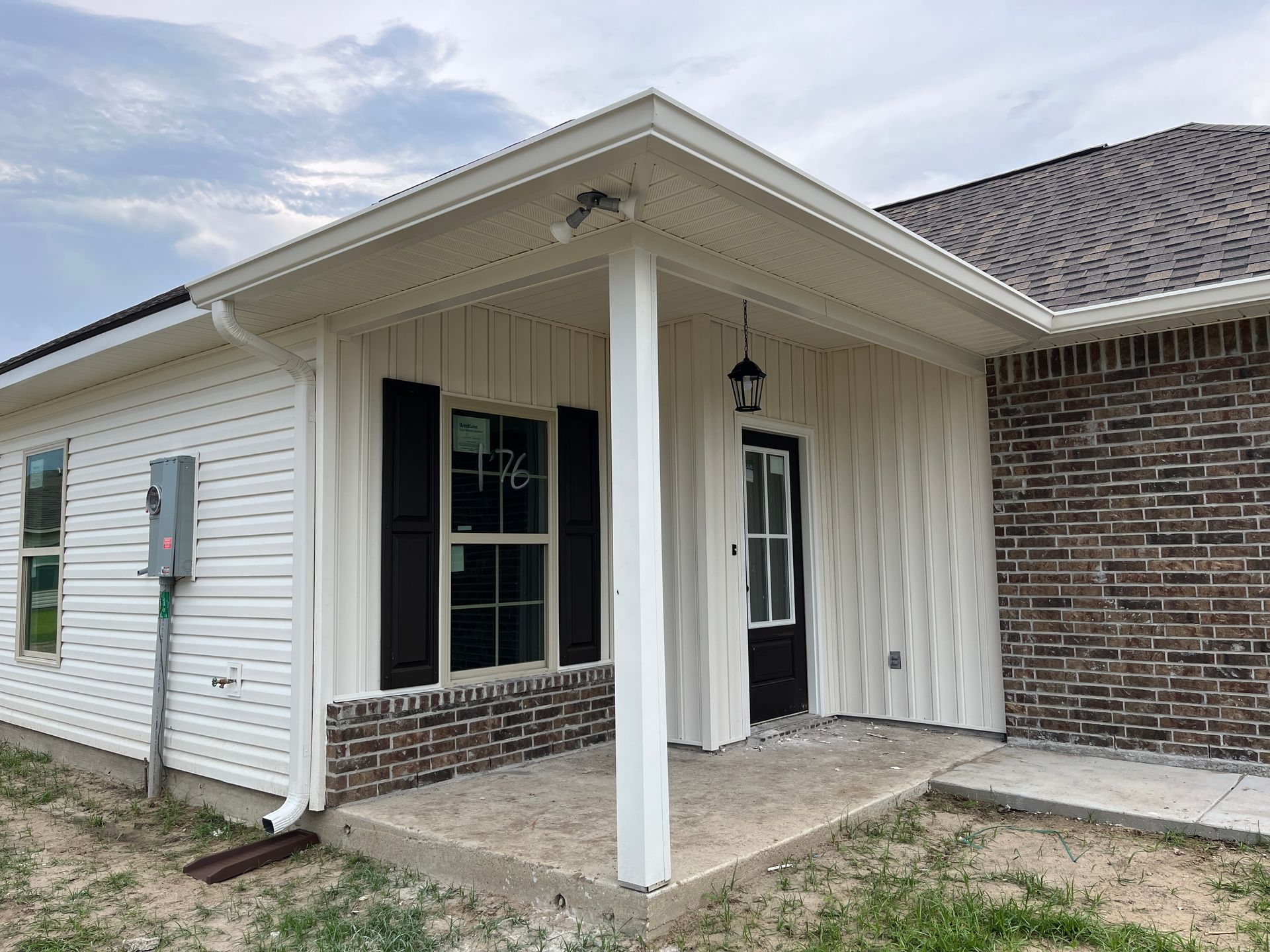 A white house with a brick base and trim, a covered porch, a black front door, and black window shutters.