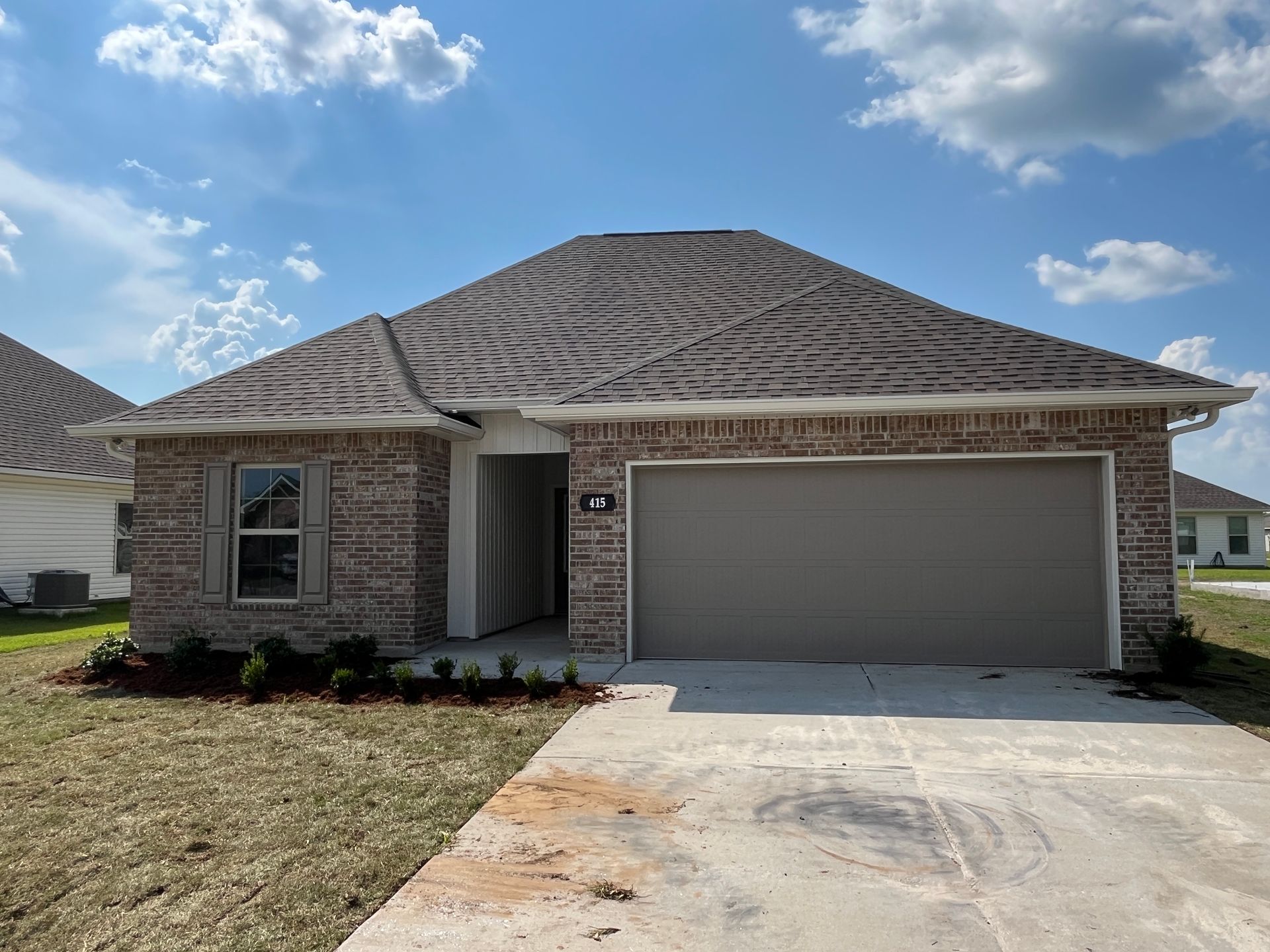 A new single-story brick house with a tan two-car garage under a bright, partly cloudy blue sky.