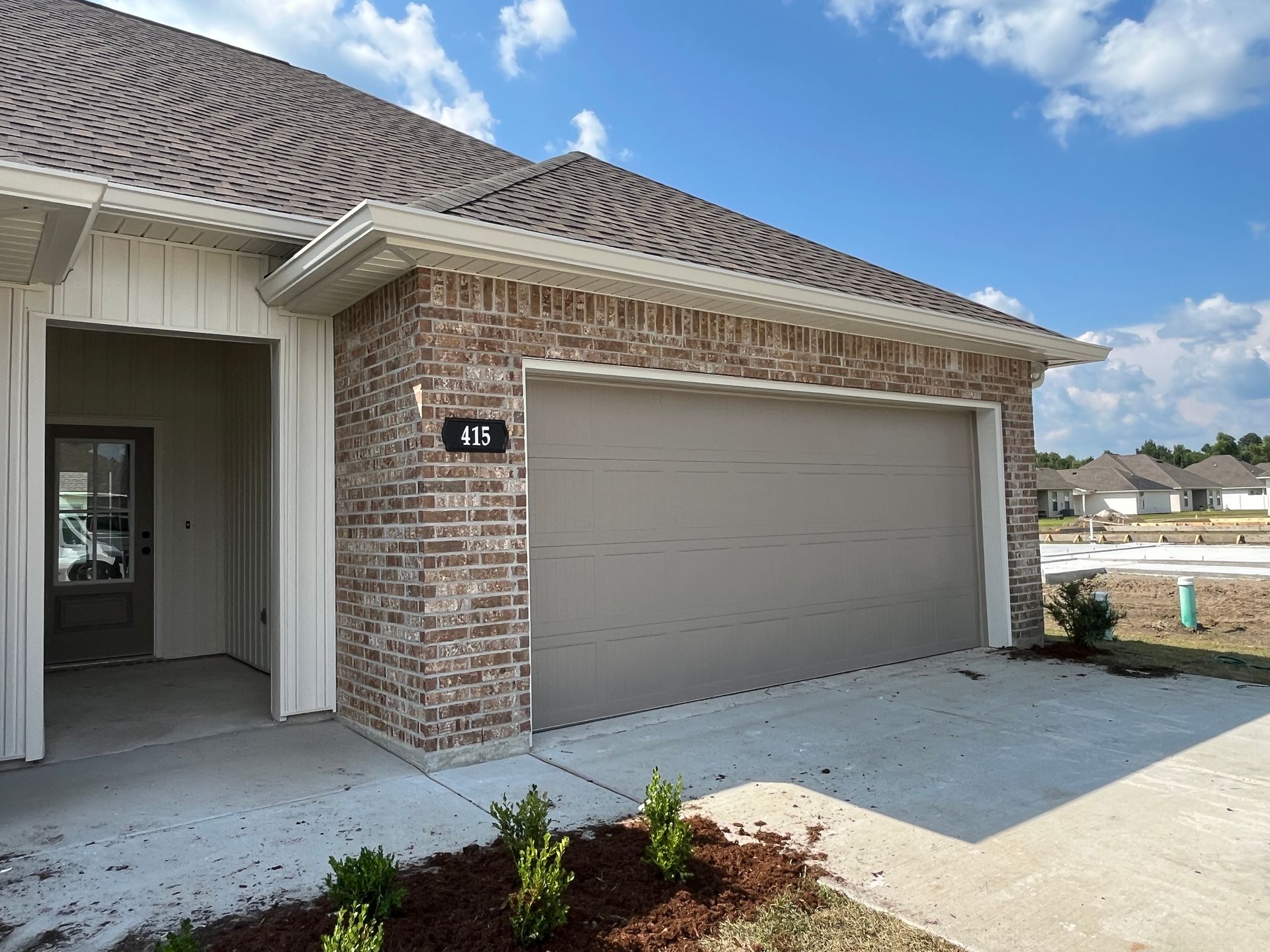Exterior of a house with a tan garage door, brick siding, and a small front entrance under a clear blue sky.