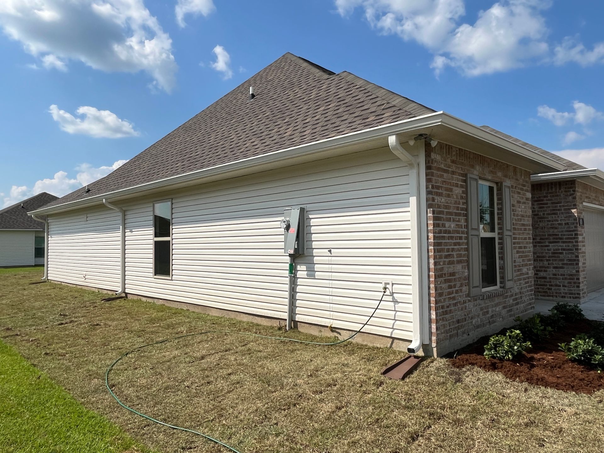 The side of a residential house featuring white vinyl siding, a brown brick front section, and a tan shingled roof.