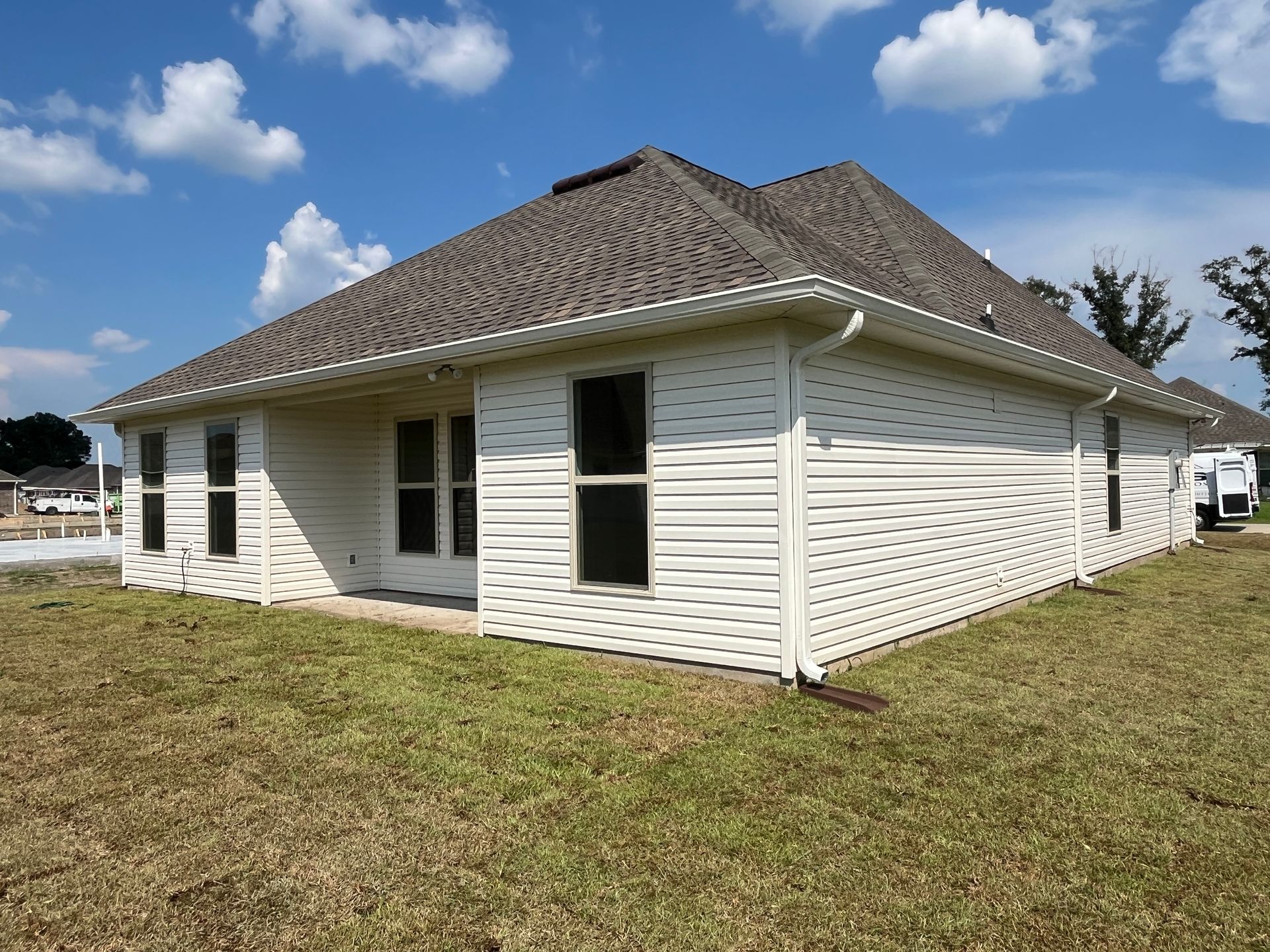 A light-colored, single-story house with a shingled roof under a bright blue sky with scattered white clouds.