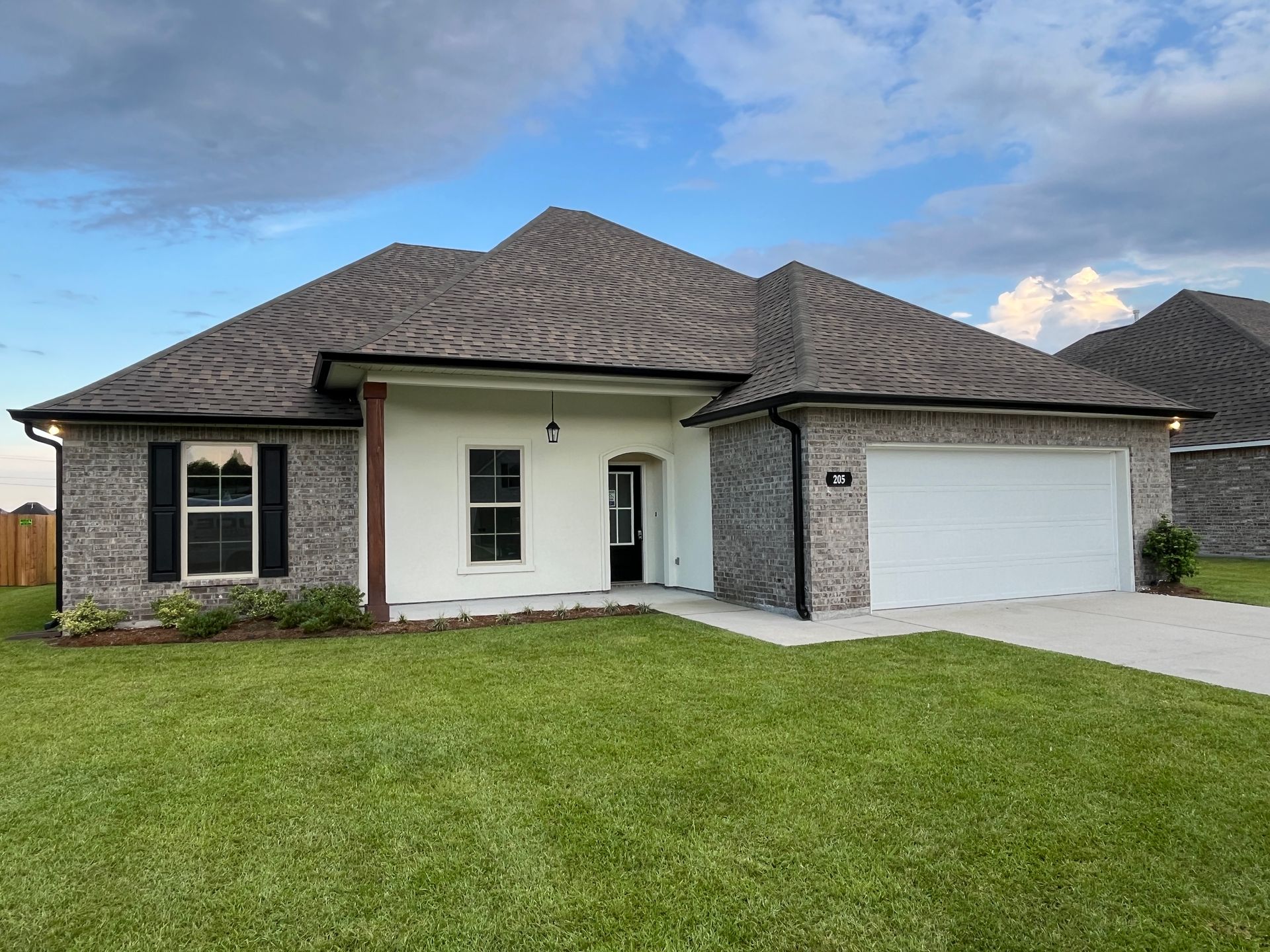 A single-story suburban house with a gray brick exterior, white siding accents, a two-car garage, and a green lawn.