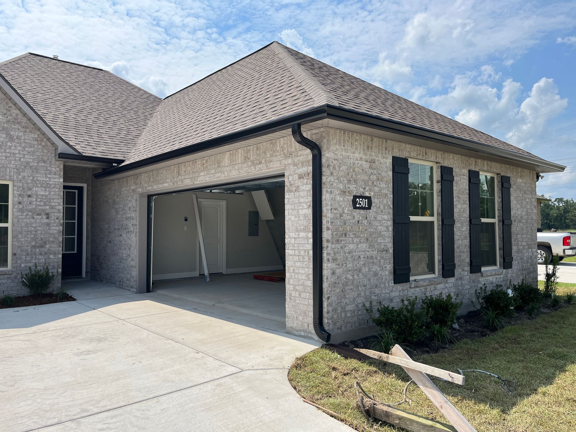 A modern, light-colored brick house exterior featuring a two-car garage with open doors and black window shutters.