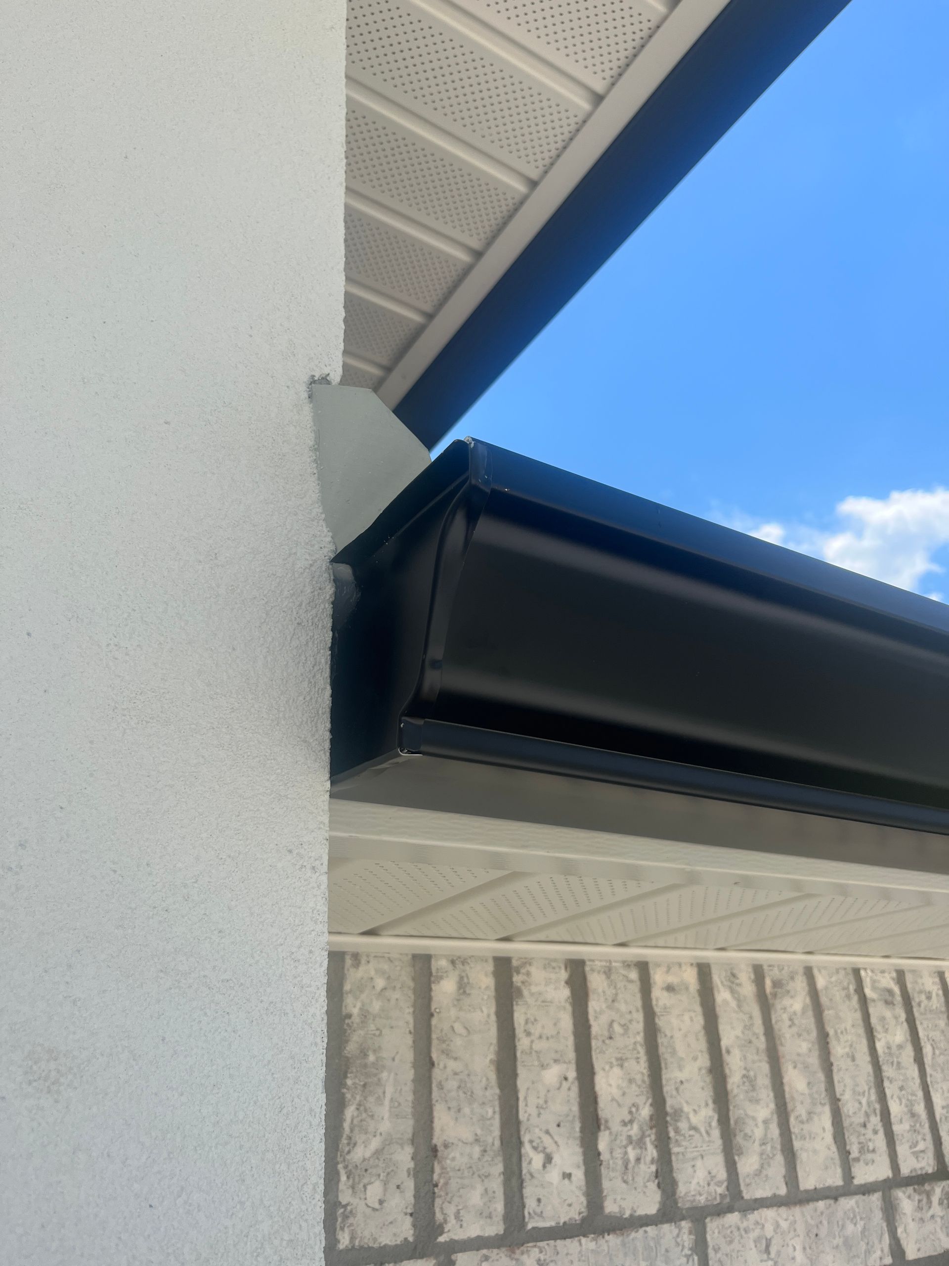 A view looking up at the corner of a house where black gutters meet a white stucco wall and a light-colored soffit.
