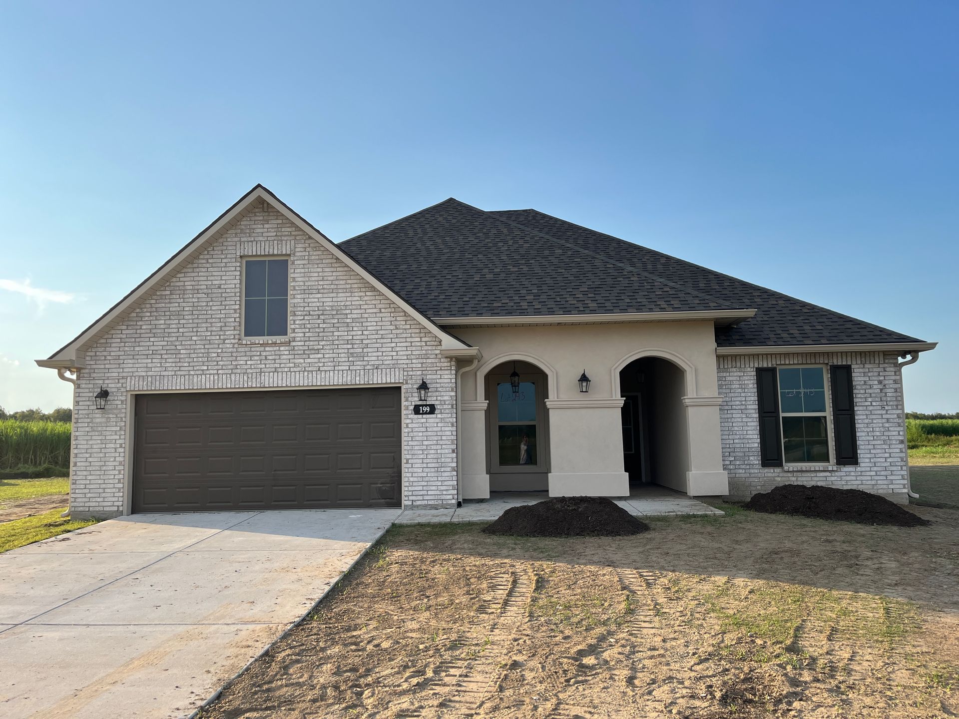 Single-story home with a white brick facade, brown garage door, dark roof, and a covered front entryway under clear skies.