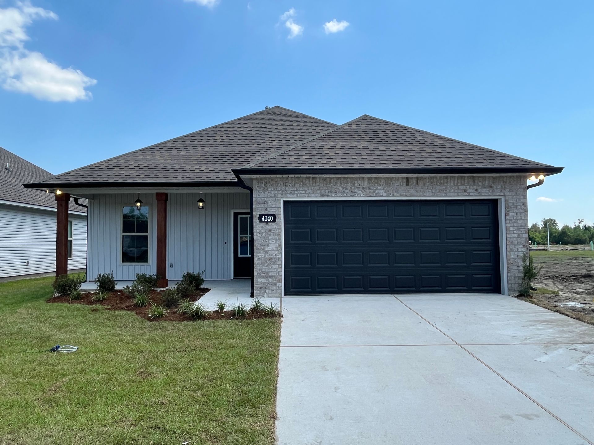 A single-story suburban house with light brick and white vertical siding, a dark garage door, and a concrete driveway.