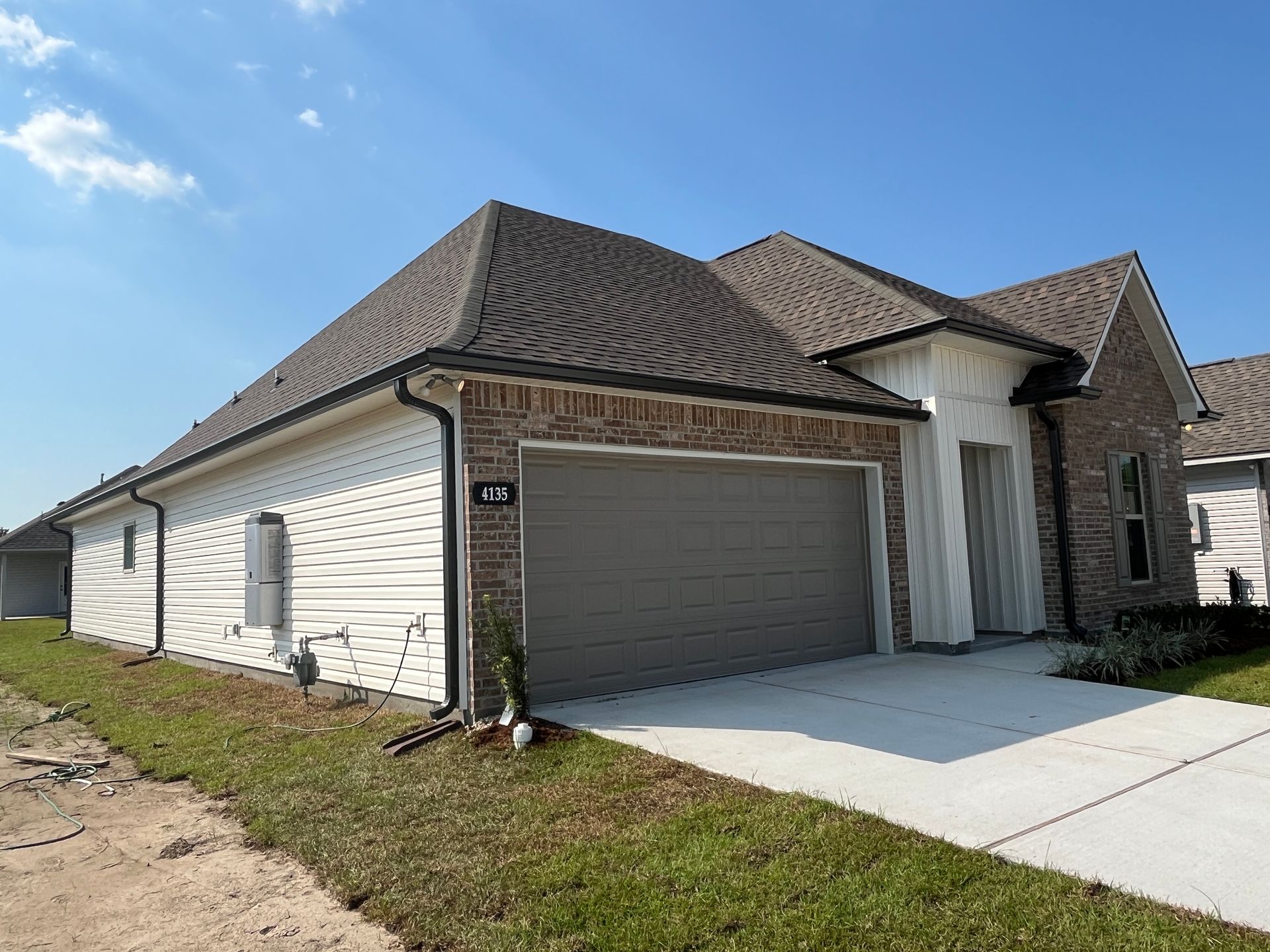 A single-story suburban house with brick and white horizontal siding, a two-car garage, and a gray shingled roof.