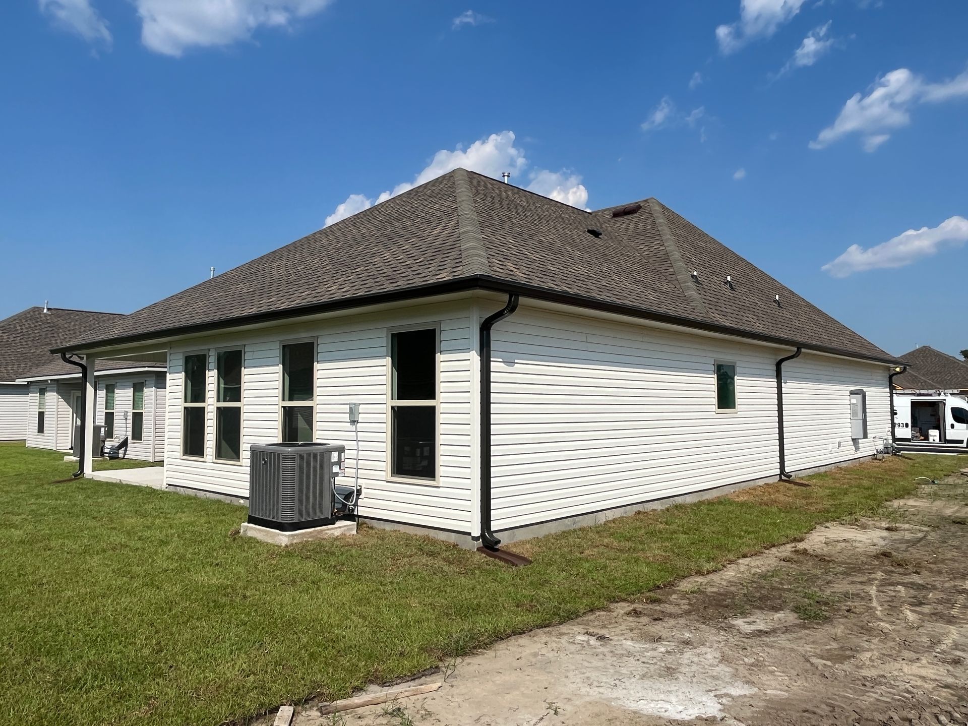 A rear view of a one-story house with light-colored horizontal siding, dark roof shingles, and an outdoor AC unit.