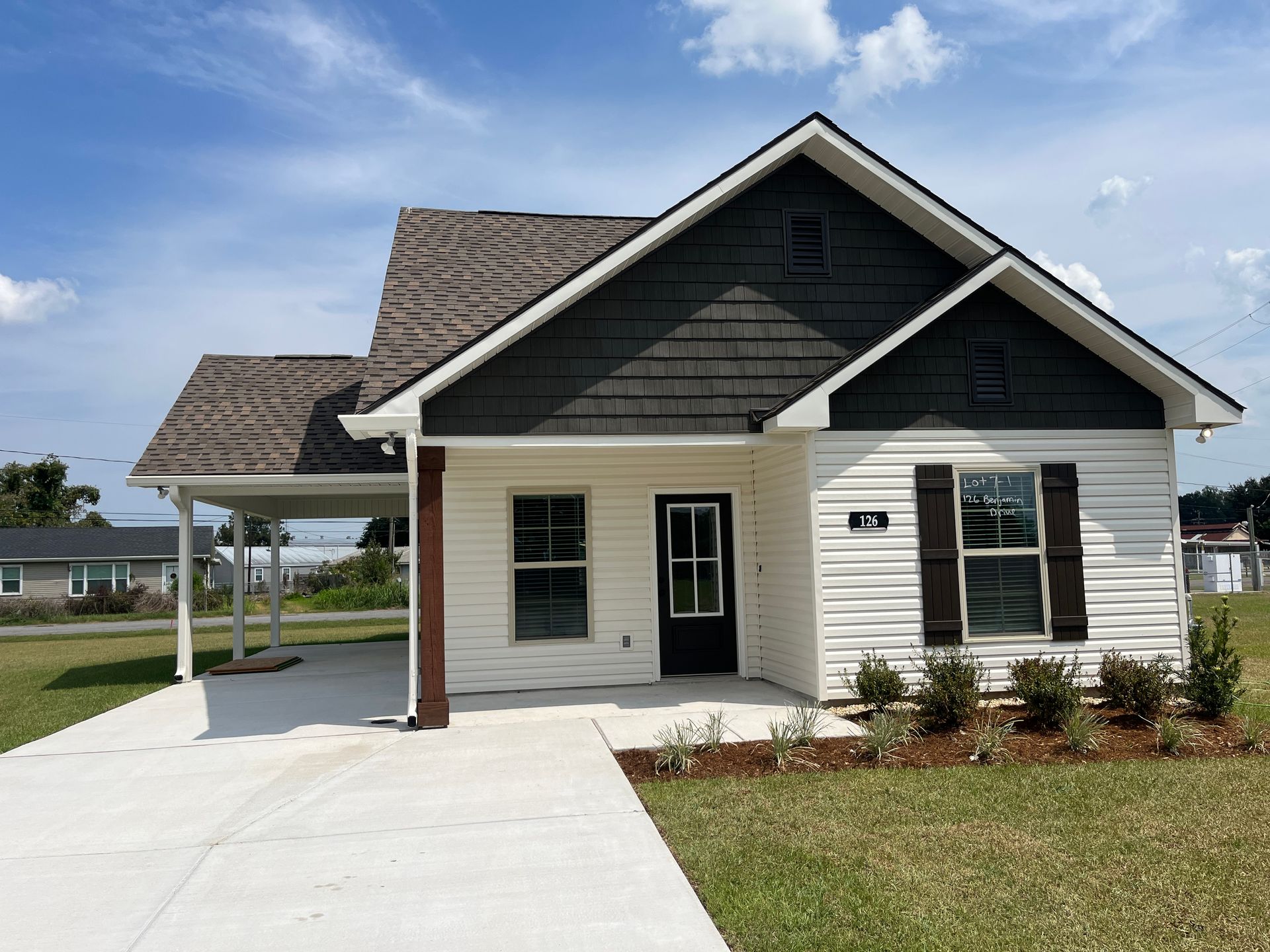A modern single-story house with cream siding, dark grey gables, and a white concrete driveway and front porch.
