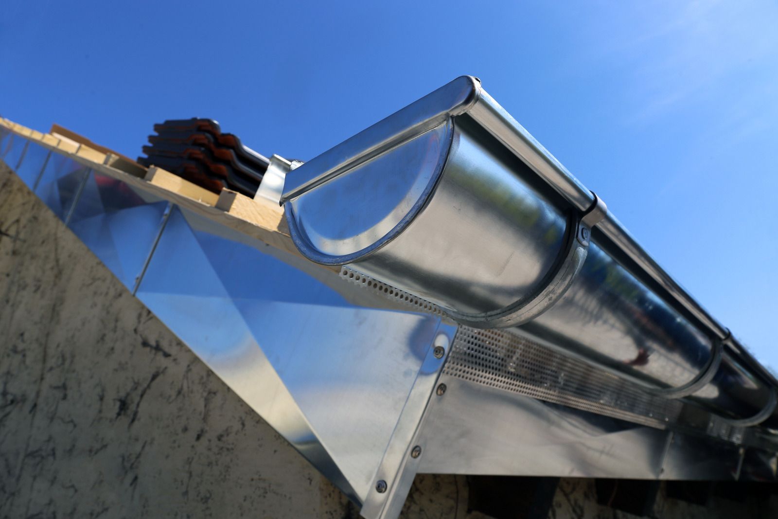 A close up of a metal gutter on a roof with a blue sky in the background.