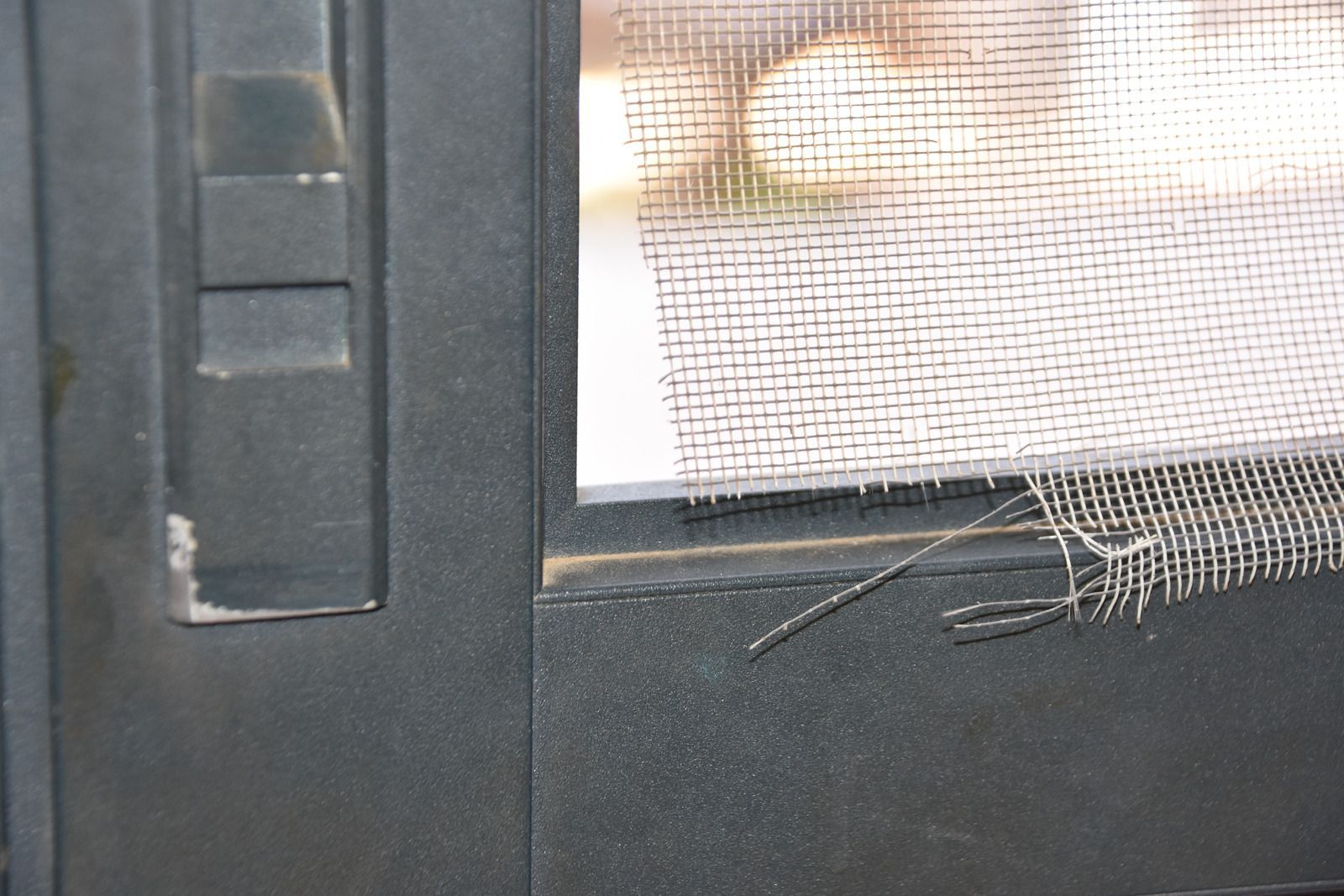 A close up of a screen door with a hole in it