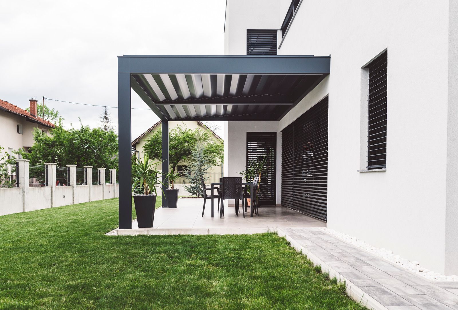 A white house with a pergola and a patio with a table and chairs.