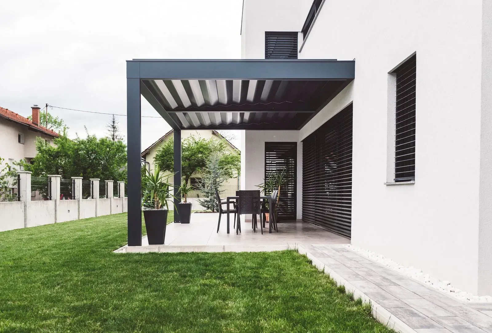 Modern white house patio with dark pergola, outdoor dining set, and green lawn