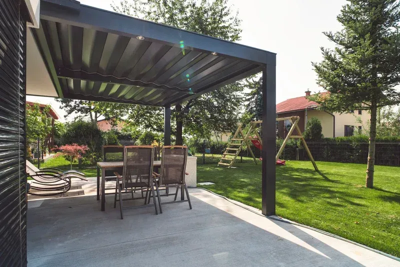 Covered driveway with a carport, concrete path, fence, trees, and a white house in the background