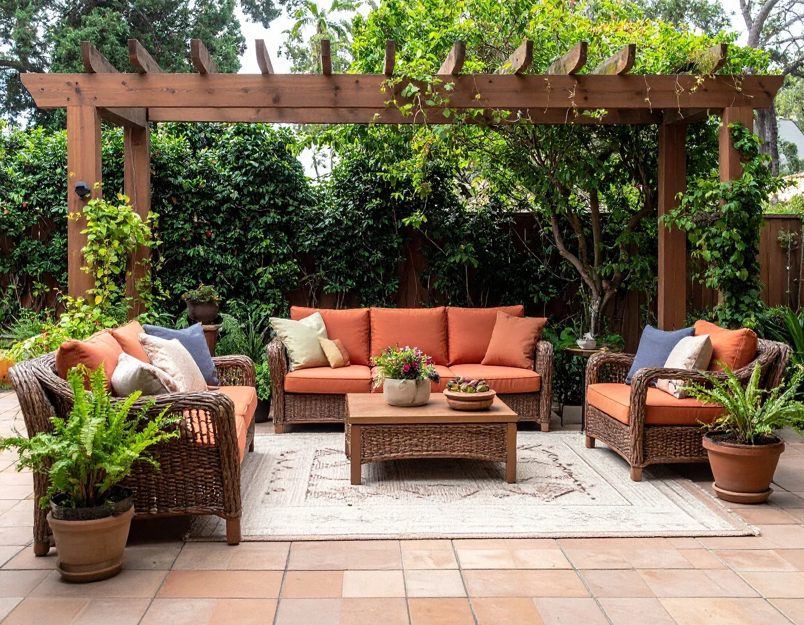 Patio with wicker furniture, orange cushions, and a wooden pergola.
