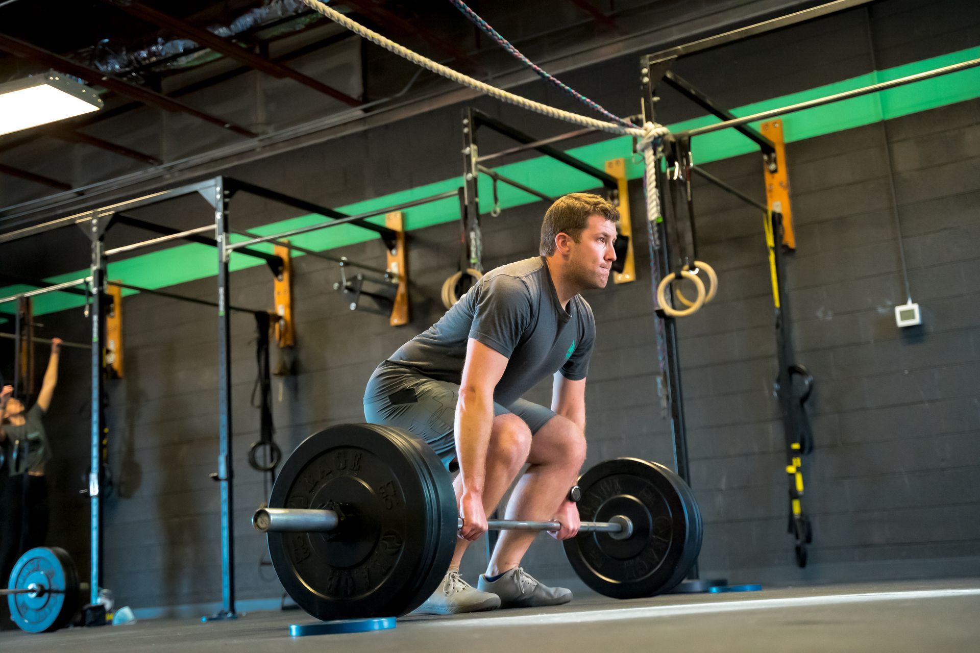 Man doing CrossFit in Lakewood, CO, deadlifting heavy barbell in gym. Dark setting with weightlifting equipment.