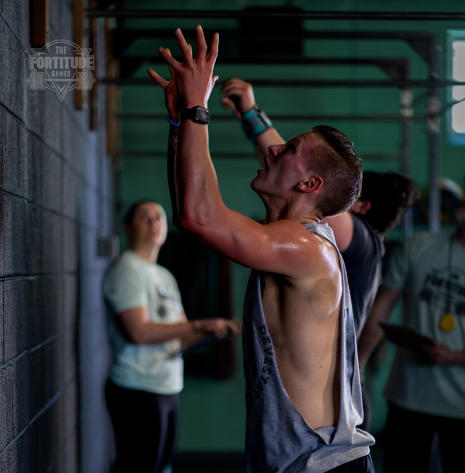 Man reaching for pull-up bar, sweaty, with onlookers, at CrossFit Common Fortitude gym in Lakewood, CO