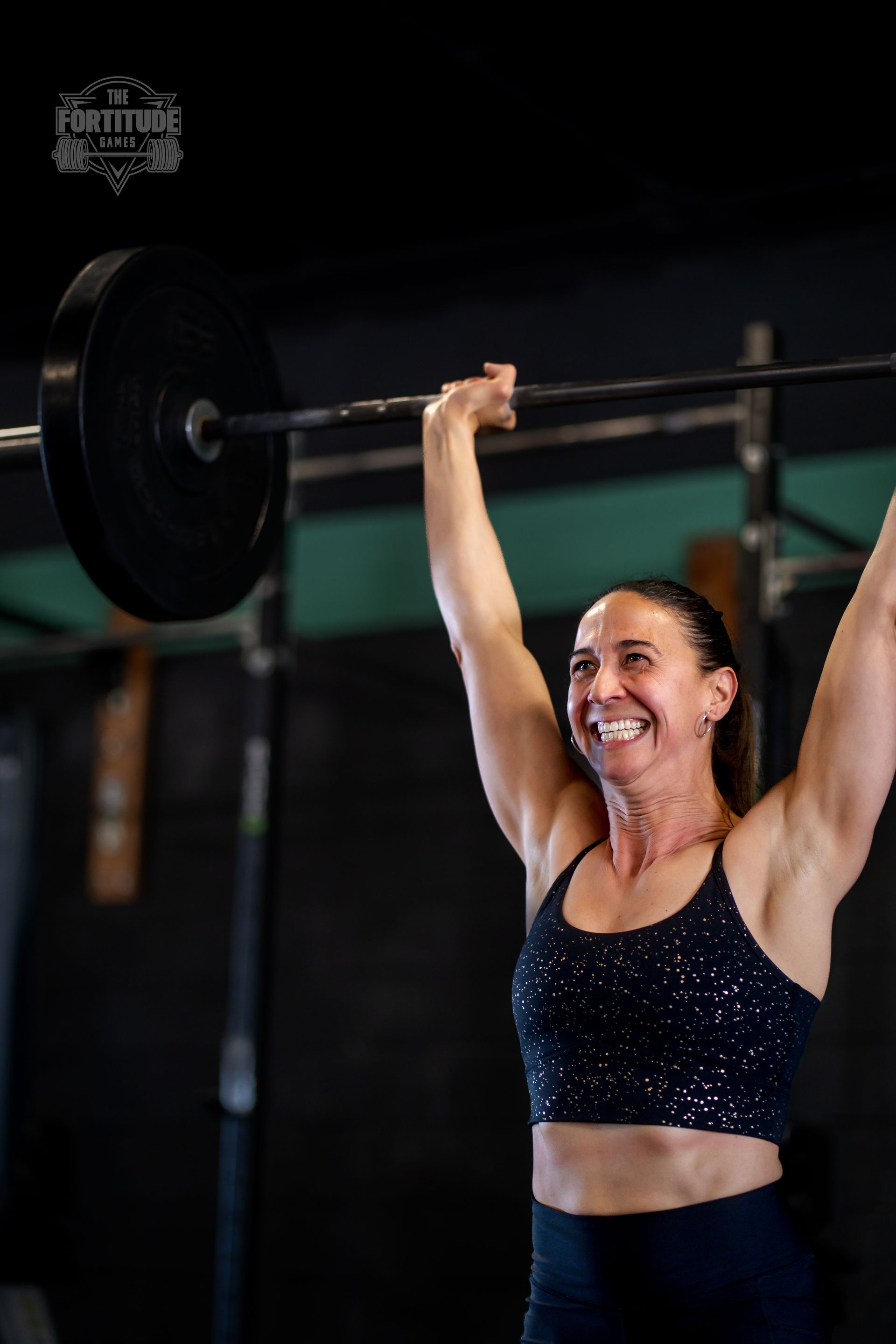 Woman smiling, lifting barbell overhead at a CrossFit gym in Lakewood, CO.