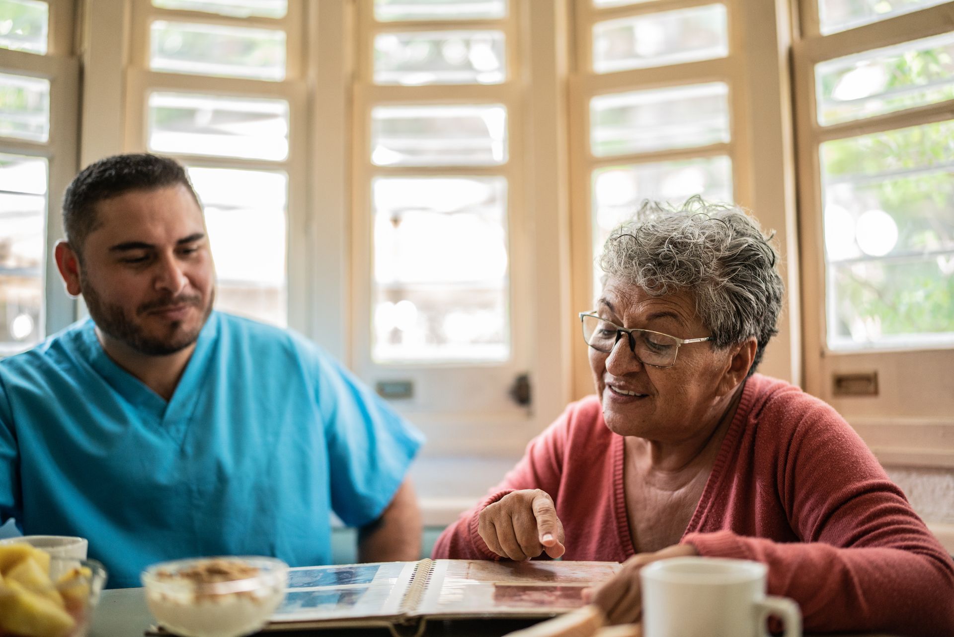 Senior woman and mid adult nurse looking at photo album in the dining room in a nursing home