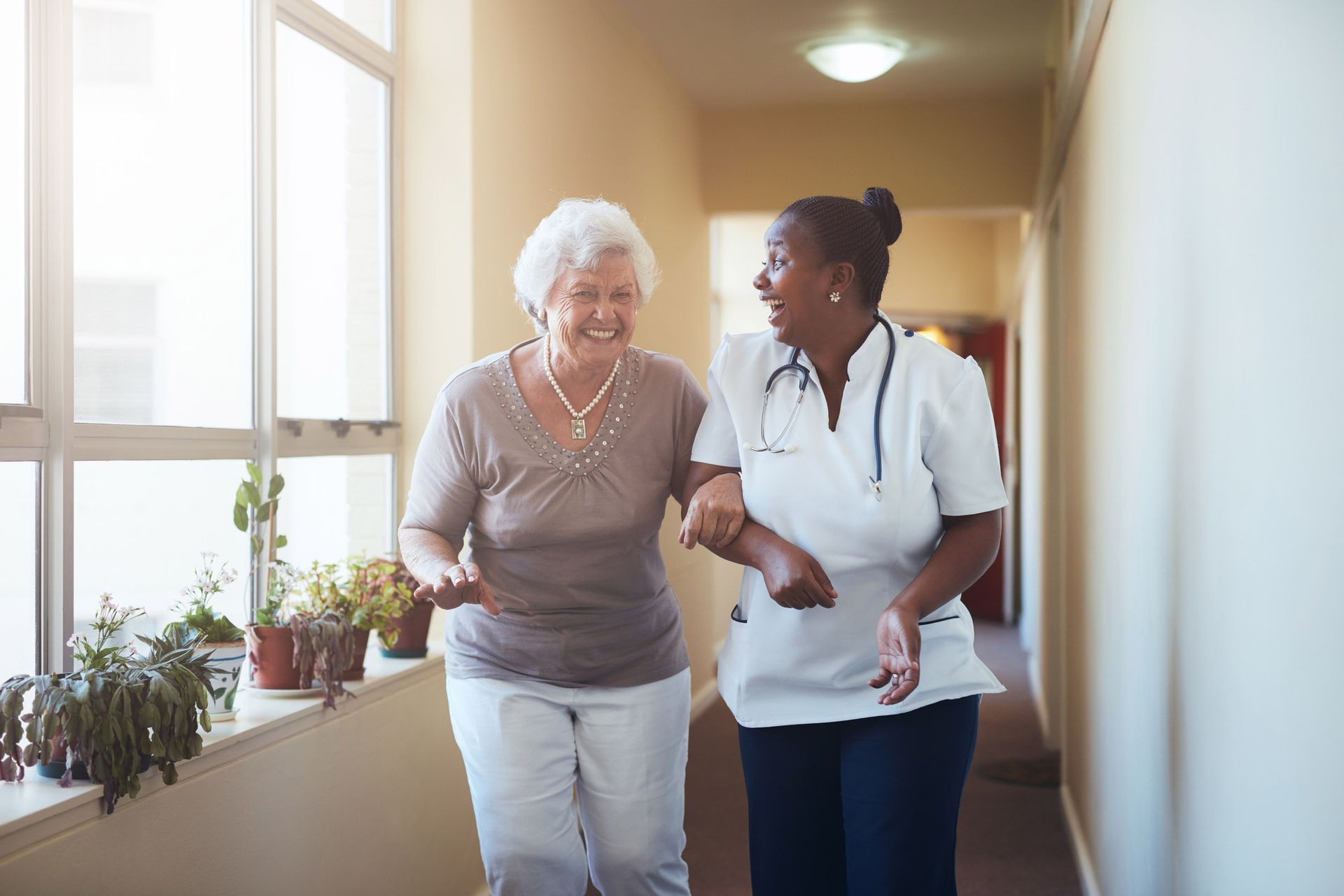 Healthcare professional assisting elderly person walking in a bright hallway. Healthcare professional assisting elderly person walking in a bright hallway.