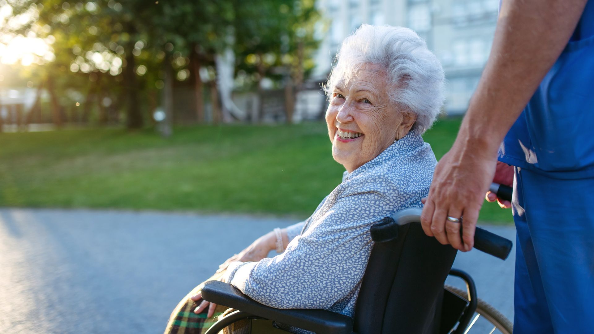 Elderly person in wheelchair outside with caregiver.