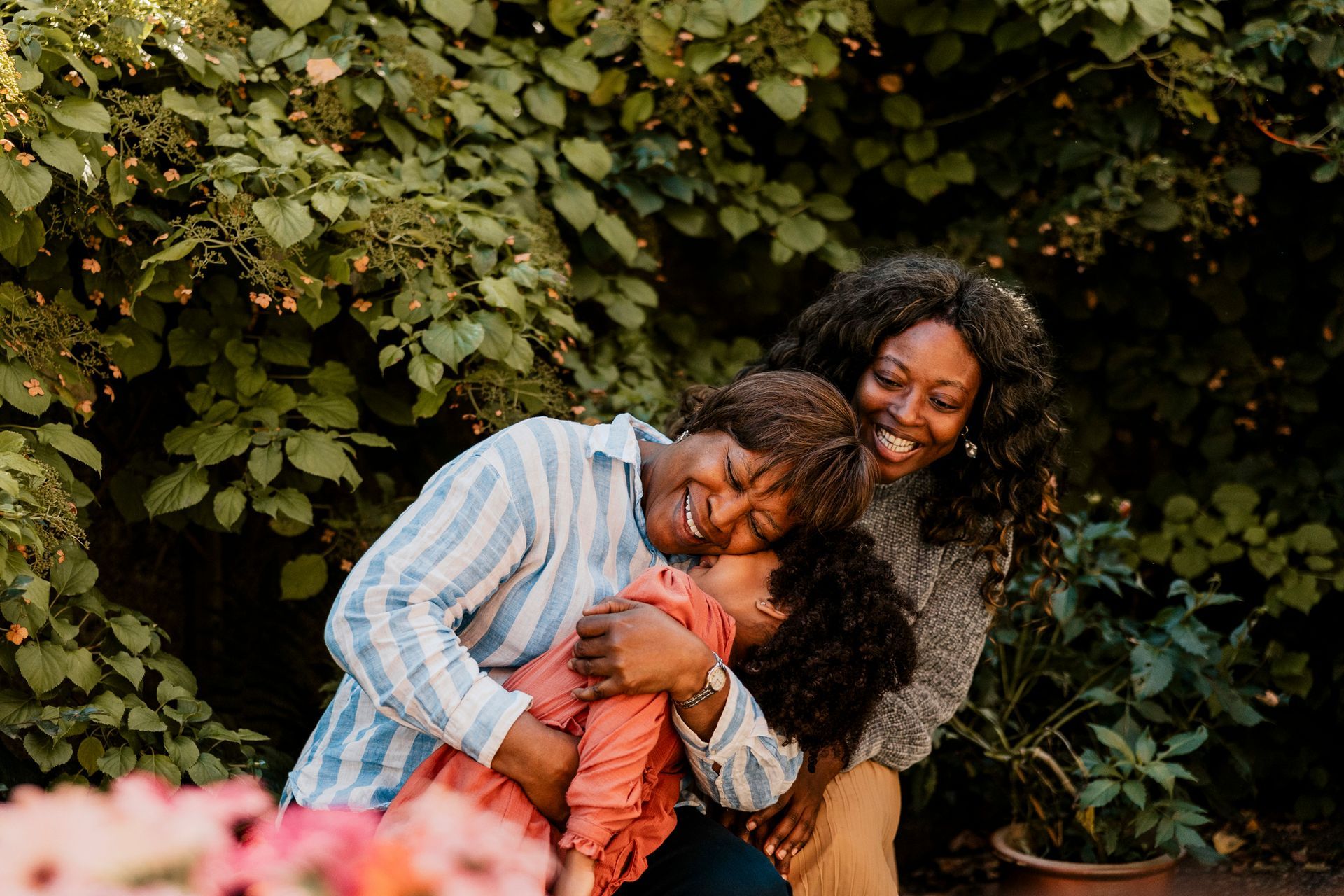 Smiling senior woman embracing granddaughter near plants in back yard. Smiling senior woman embracing granddaughter near plants in back yard.