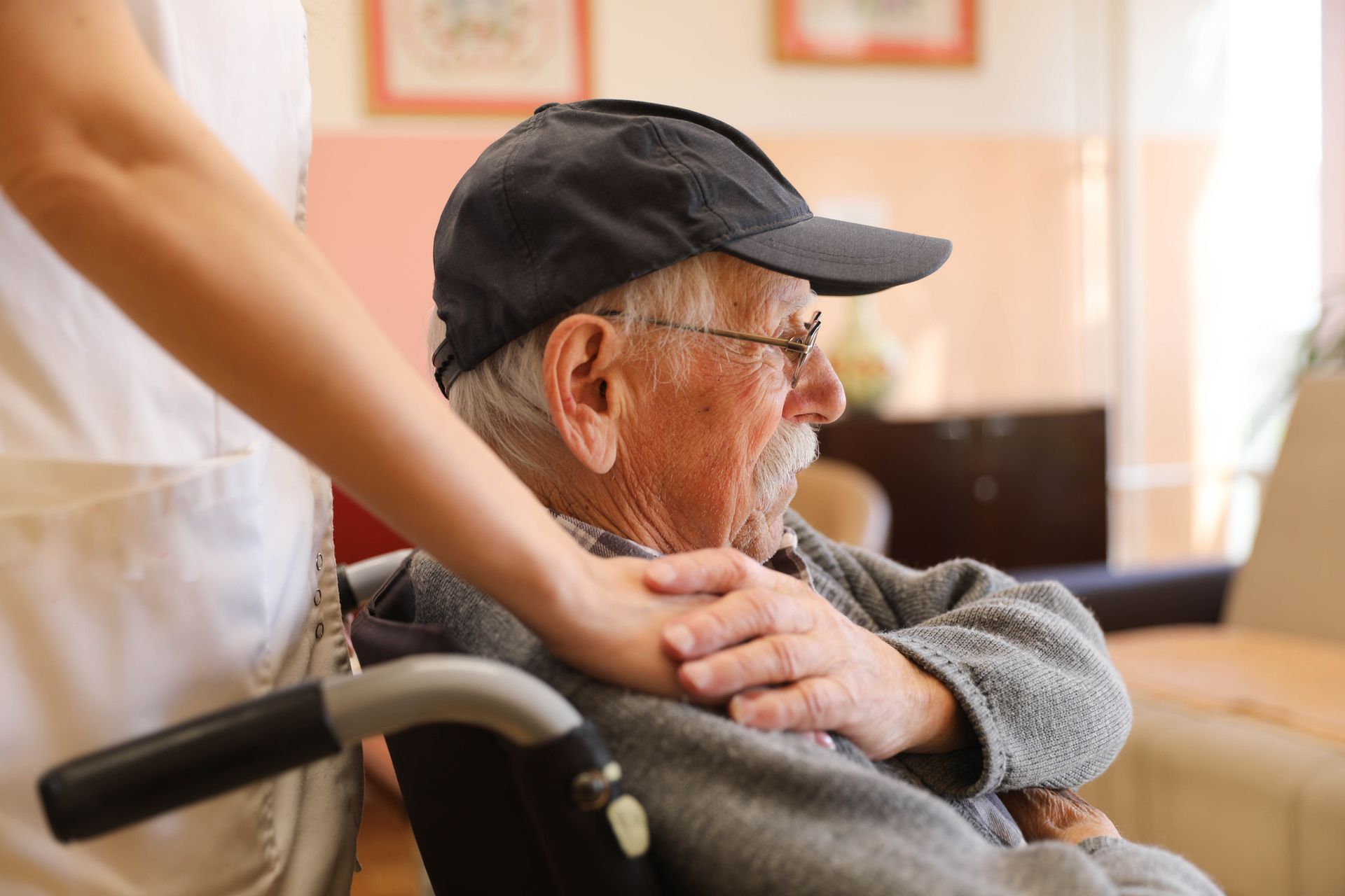 Elderly person in wheelchair with caregiver indoors.