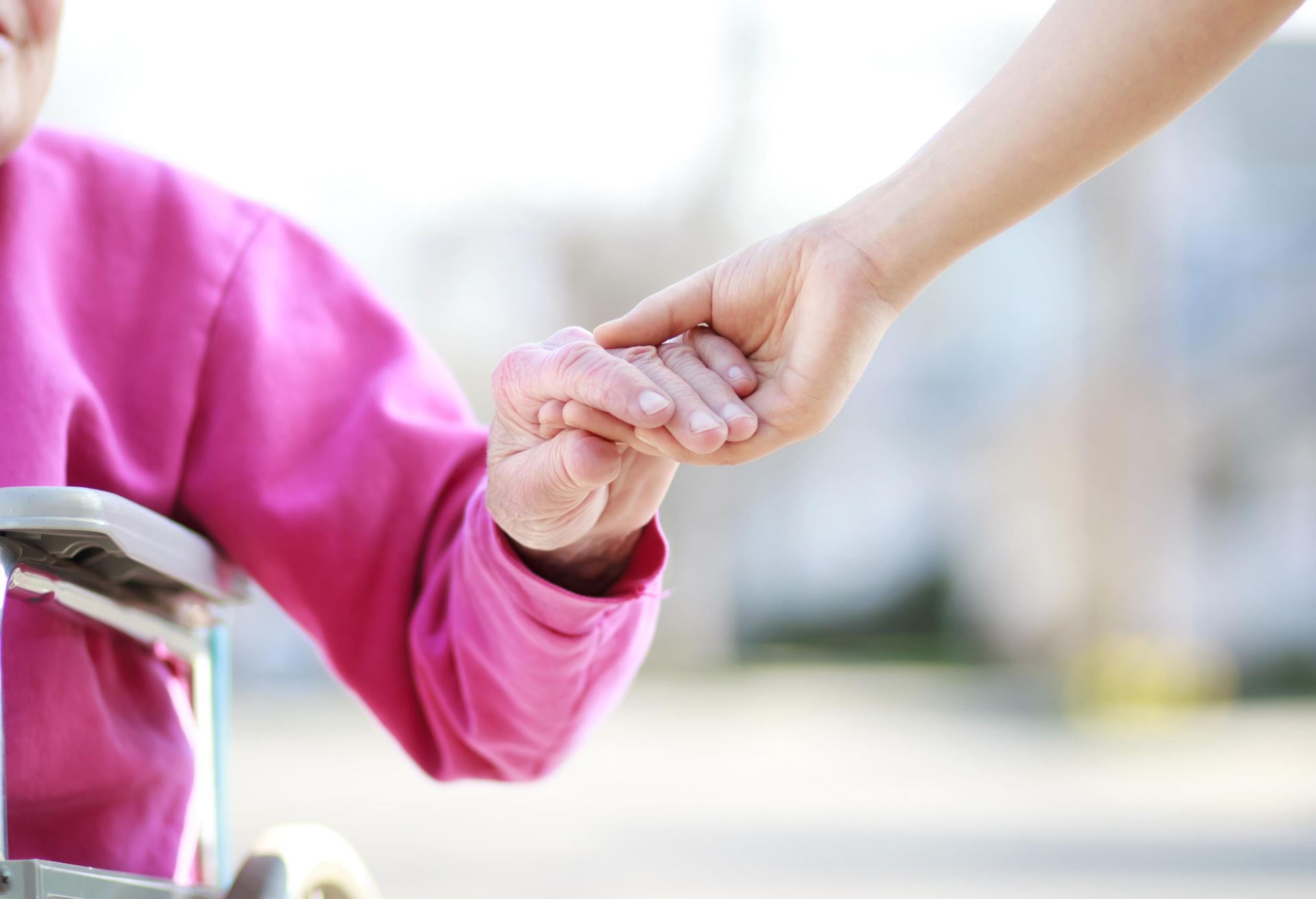 Caregiver holding hand of elderly person in wheelchair outdoors.