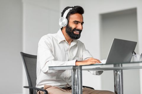 a man wearing headphones is sitting at a desk using a laptop computer .