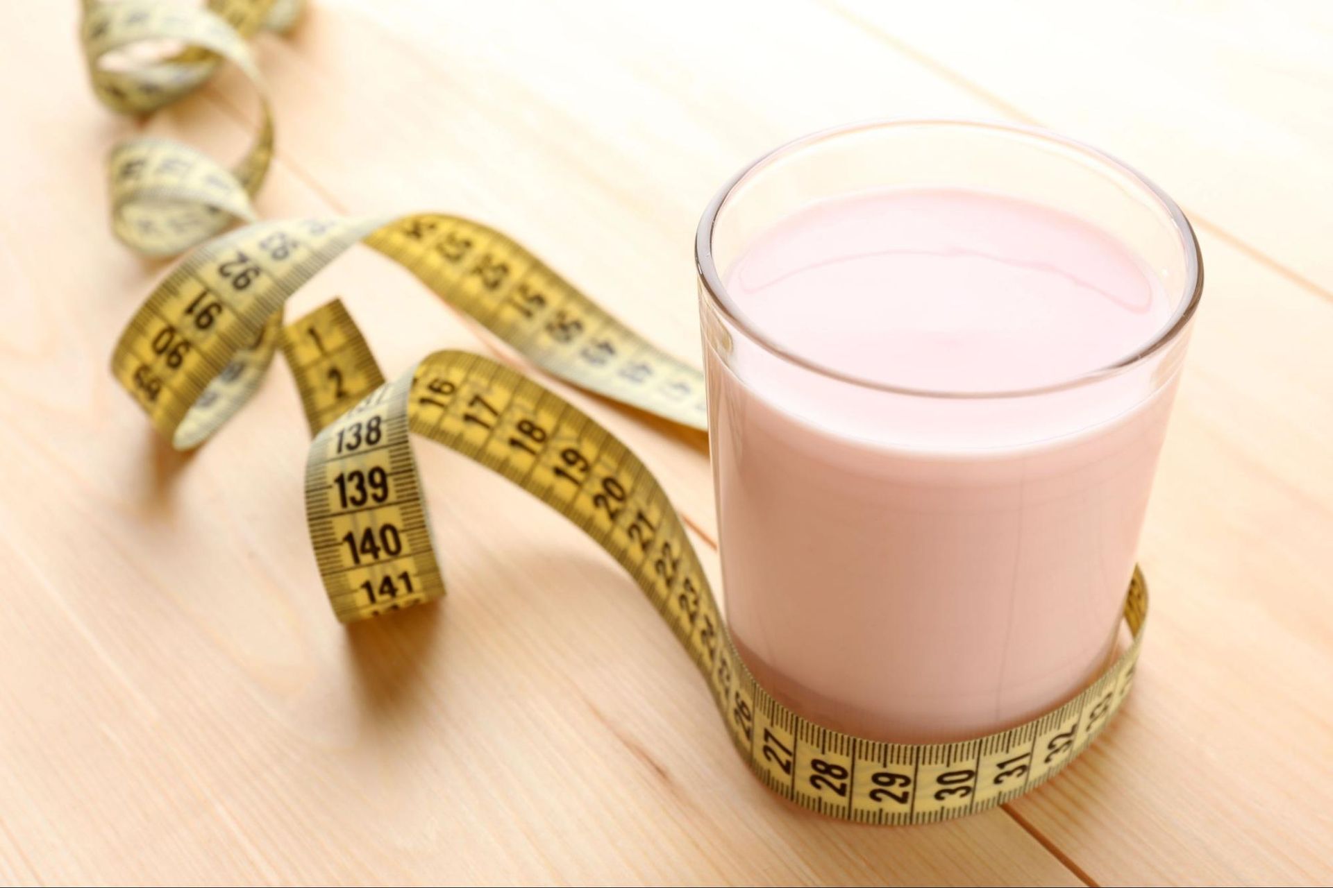 A very low-energy glass of pink meal replacement shake surrounded by a yellow measuring tape