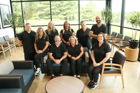 Group of dental professionals in black scrubs, smiling, posing in a waiting room with modern furniture.