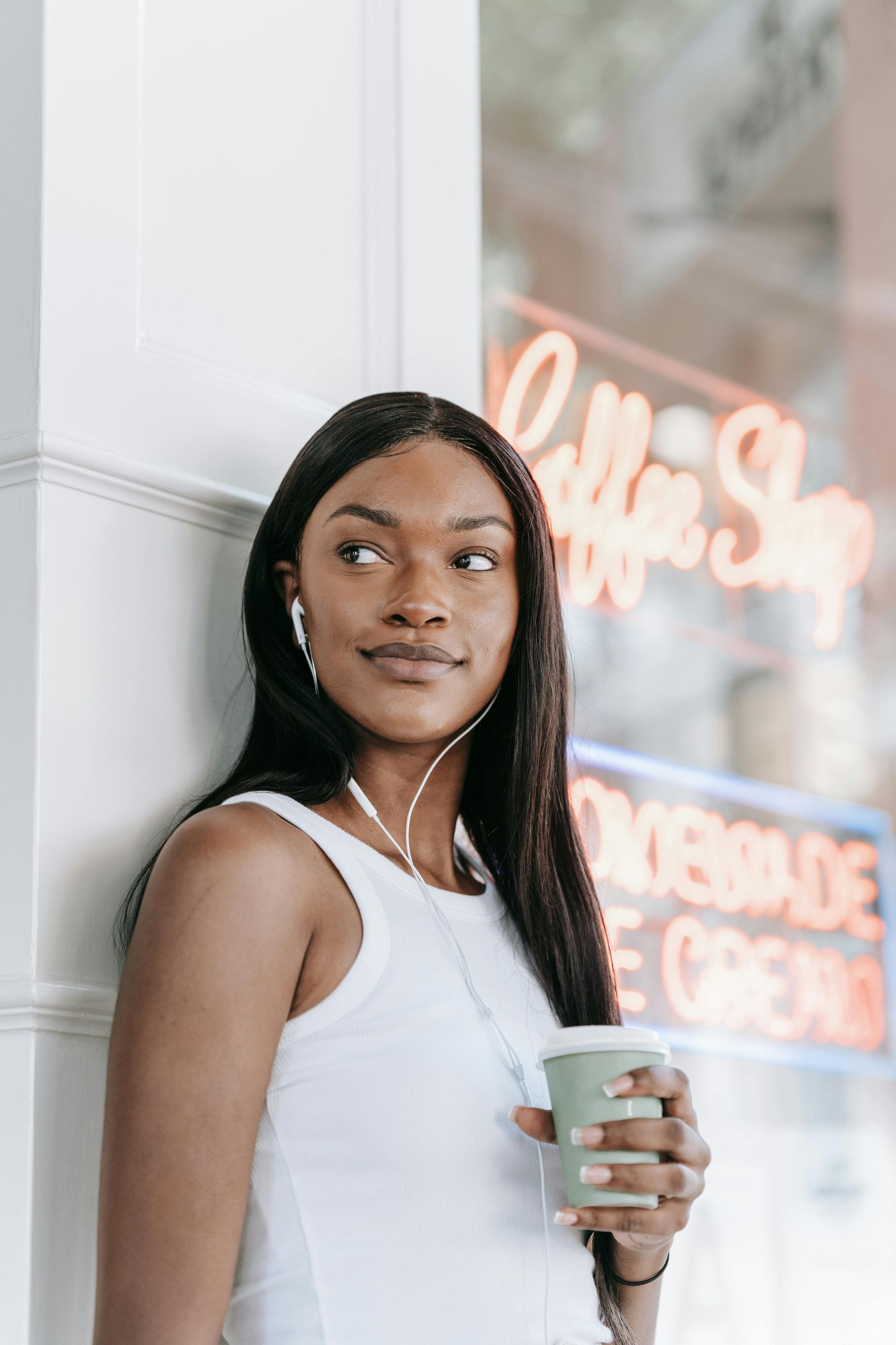 Woman in white top holding a cup beside a neon storefront window