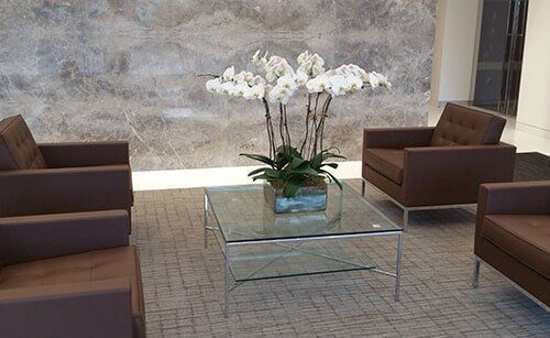 Modern lounge seating with brown chairs around a glass coffee table and white orchids on a tiled floor.
