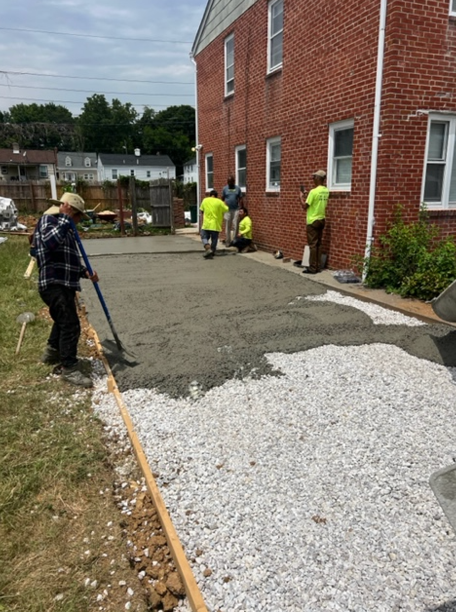 A group of construction workers are working on a driveway in front of a brick building.