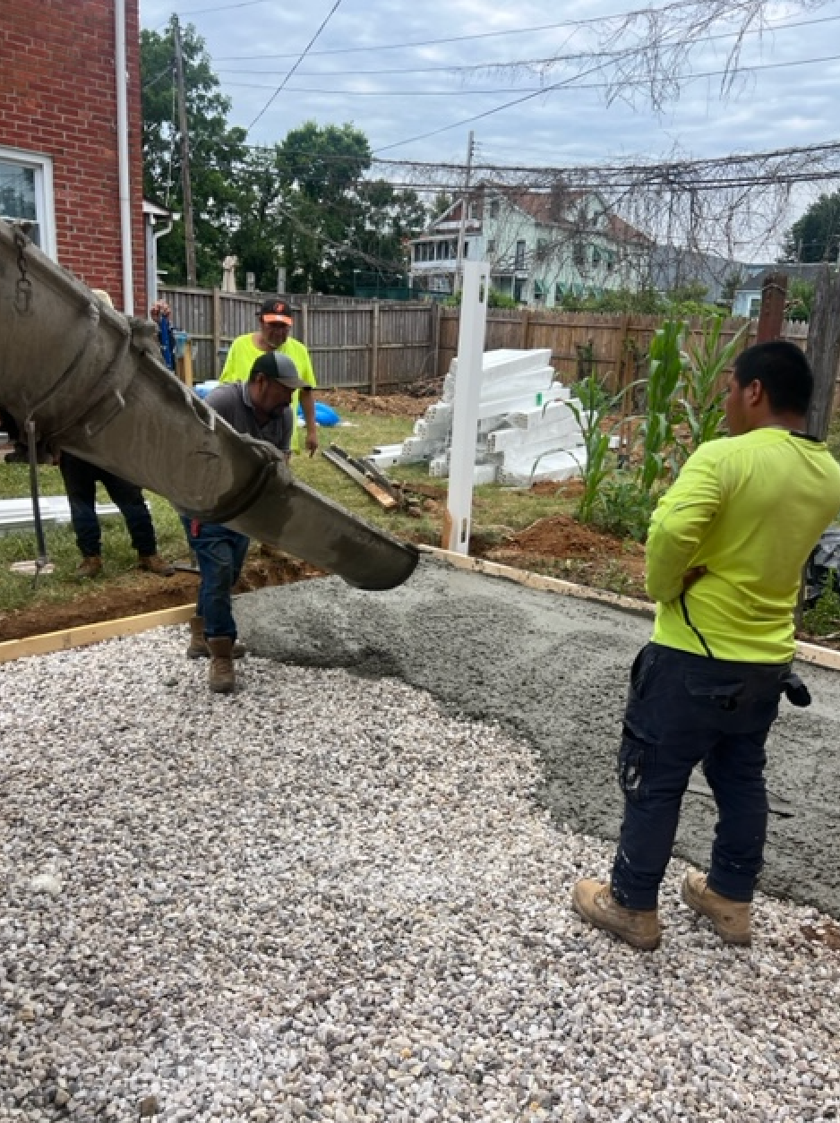 A group of construction workers are pouring concrete into a gravel driveway.