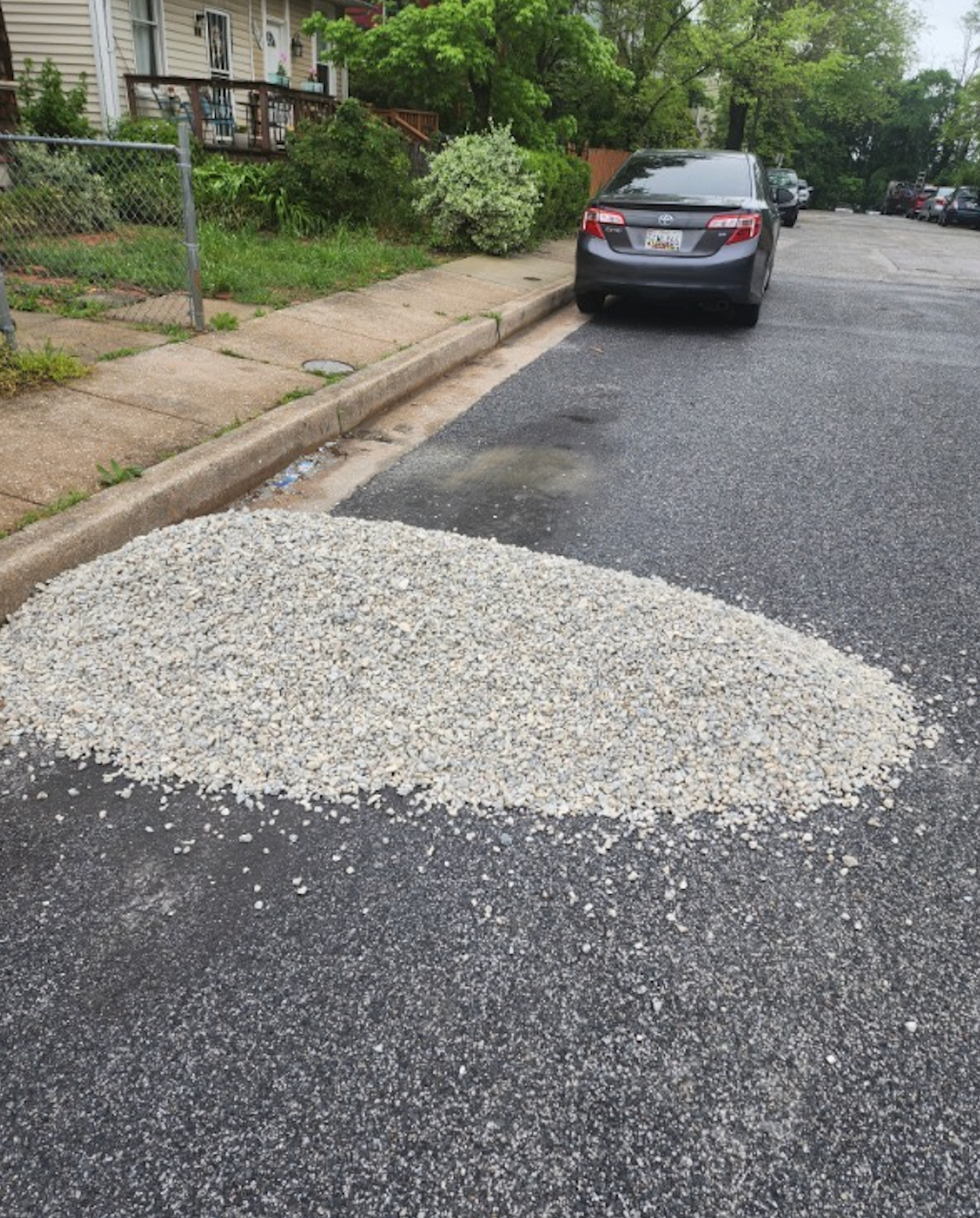 A car is parked on the side of the road next to a pile of gravel.