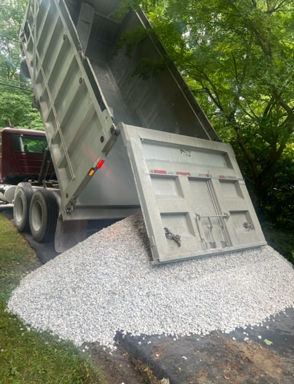 A dump truck is dumping gravel on the ground.