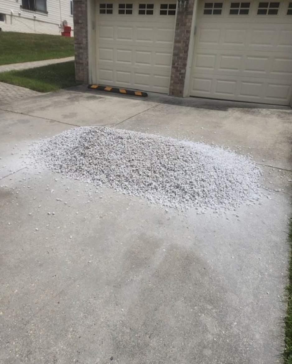 A pile of gravel is on the sidewalk in front of a garage door.